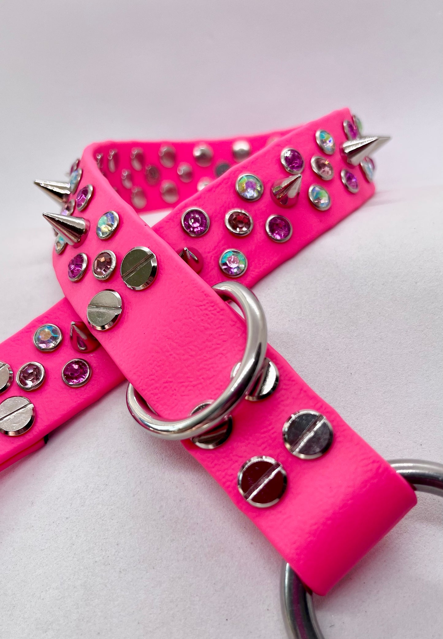 Neon pink BioThane dog collar coiled showing mixed AB crystal and pink rhinestone studs with spike detail