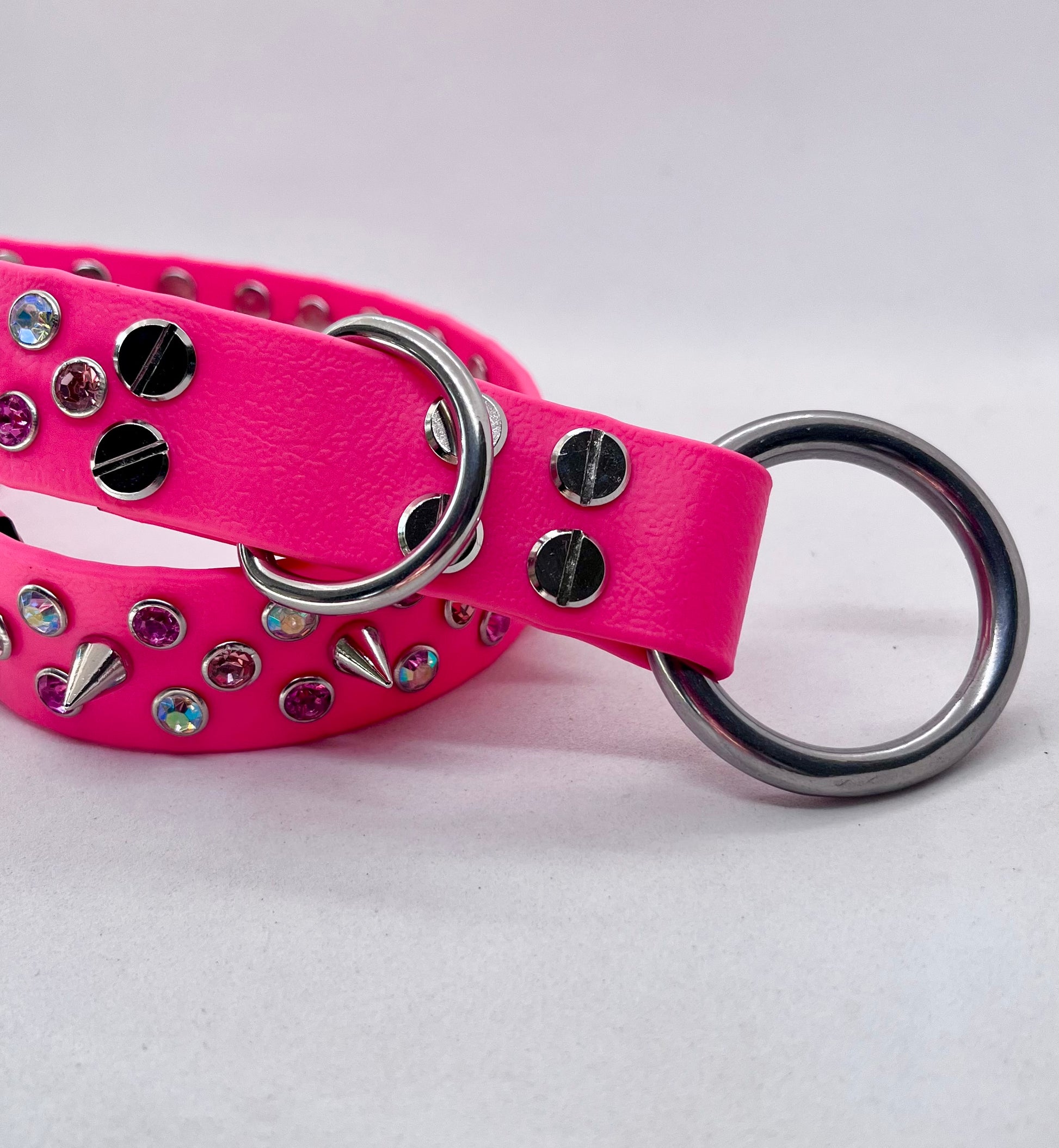 Close-up of neon pink BioThane dog collar showing stainless steel O ring, rhinestone crystals and spike studs
