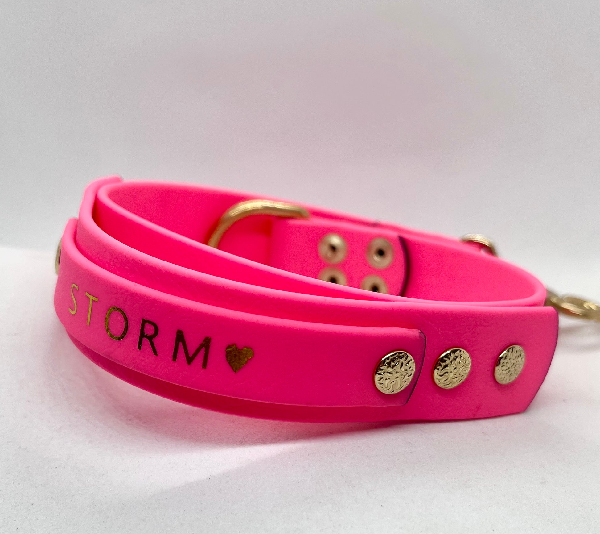 A bright pink dog collar with gold hardware, featuring the word 'STORM' and a small heart foiled on the front. JOOLS LONDON