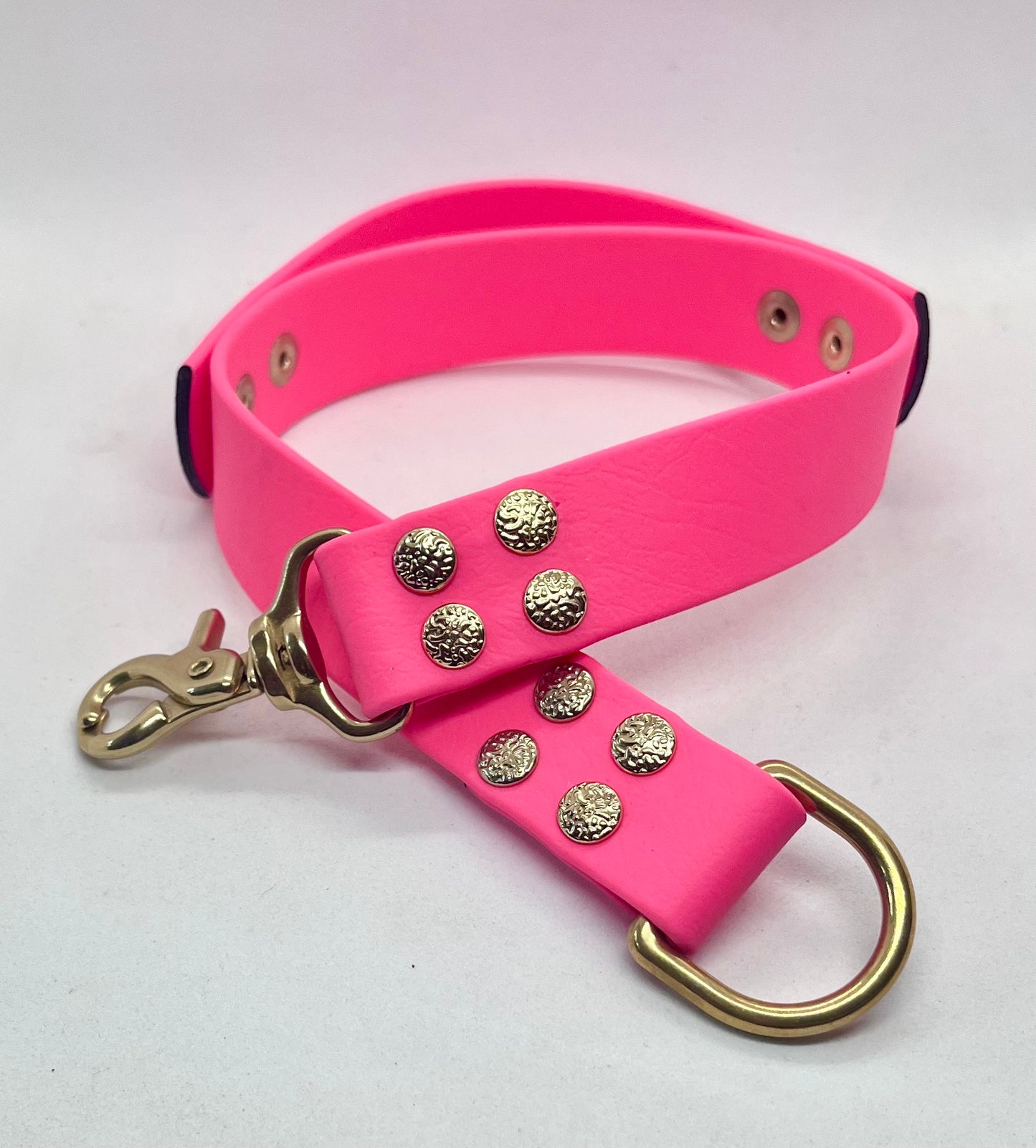 A bright pink collar featuring decorative textured gold-tone textured studs and brass hardware including a large D-ring. JOOLS LONDON