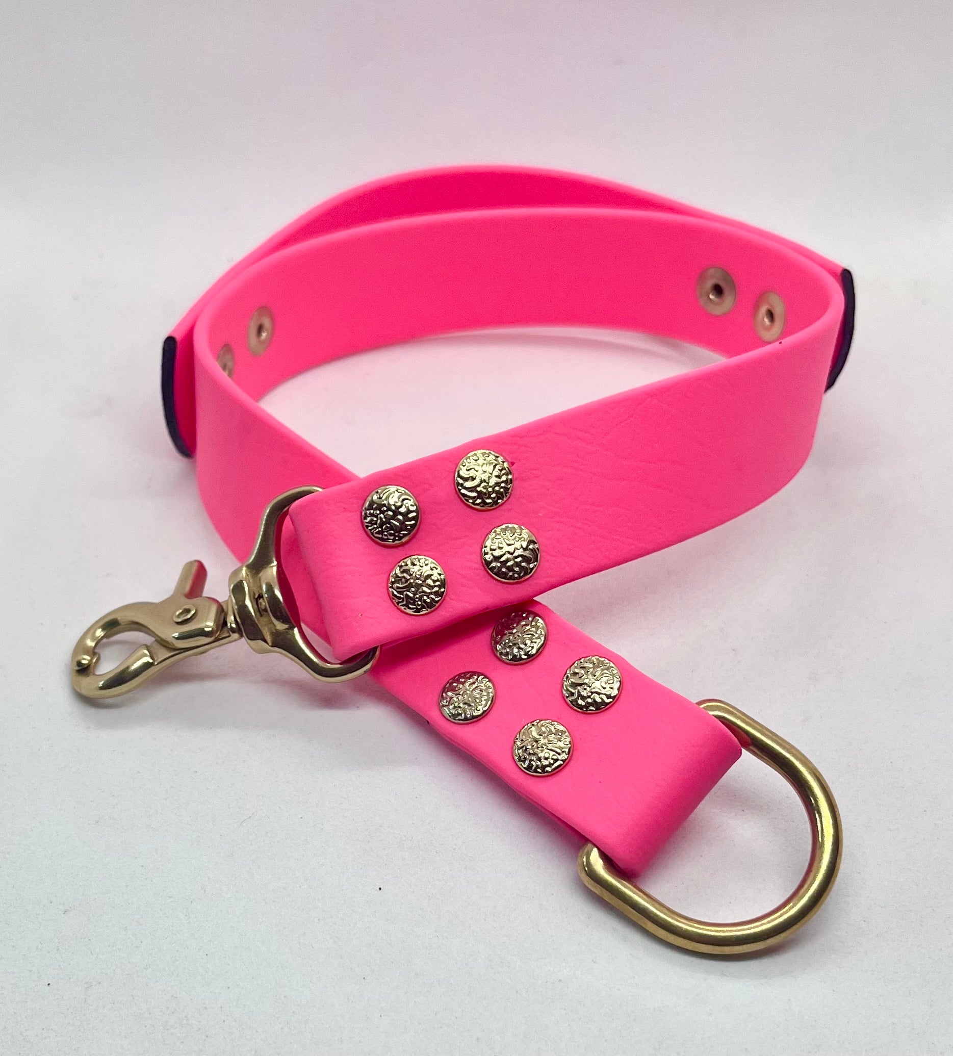 A bright pink collar featuring decorative textured gold-tone textured studs and brass hardware including a large D-ring. JOOLS LONDON