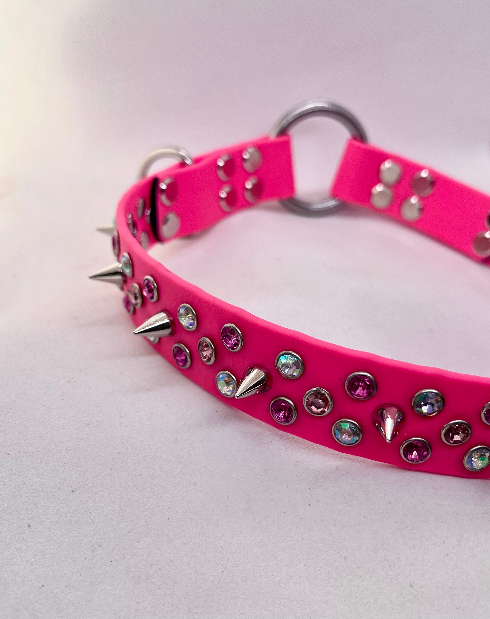 Angled close-up of neon pink spiked rhinestone BioThane dog collar with stainless steel O ring