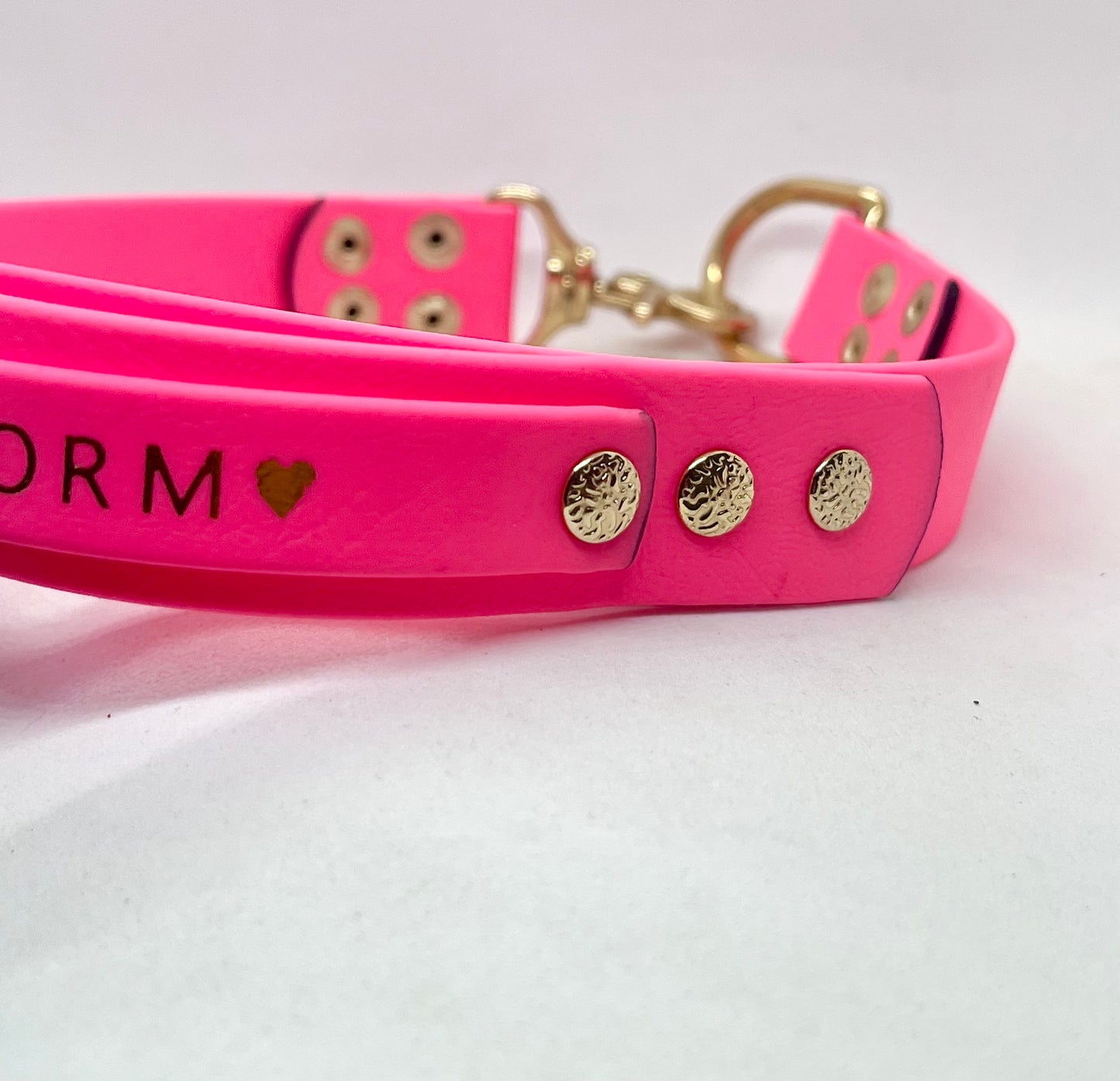 A close-up of a bright pink collar with brass hardware, including a D-ring, clasp, and decorative studs. The collar has personalised foil embossing. JOOLS LONDON