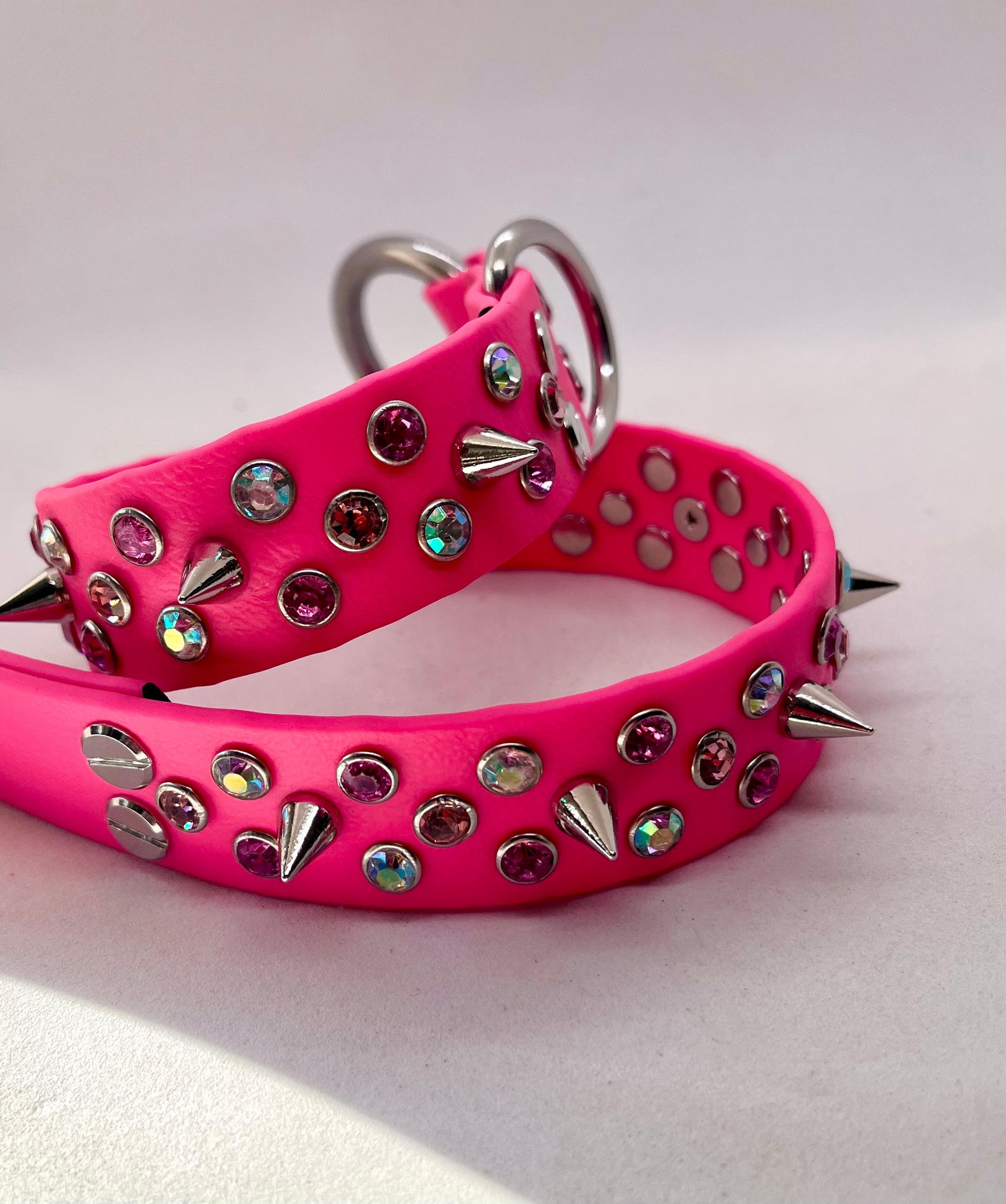 Neon pink BioThane dog collar coiled showing rhinestone crystals, spikes and stainless steel hardware