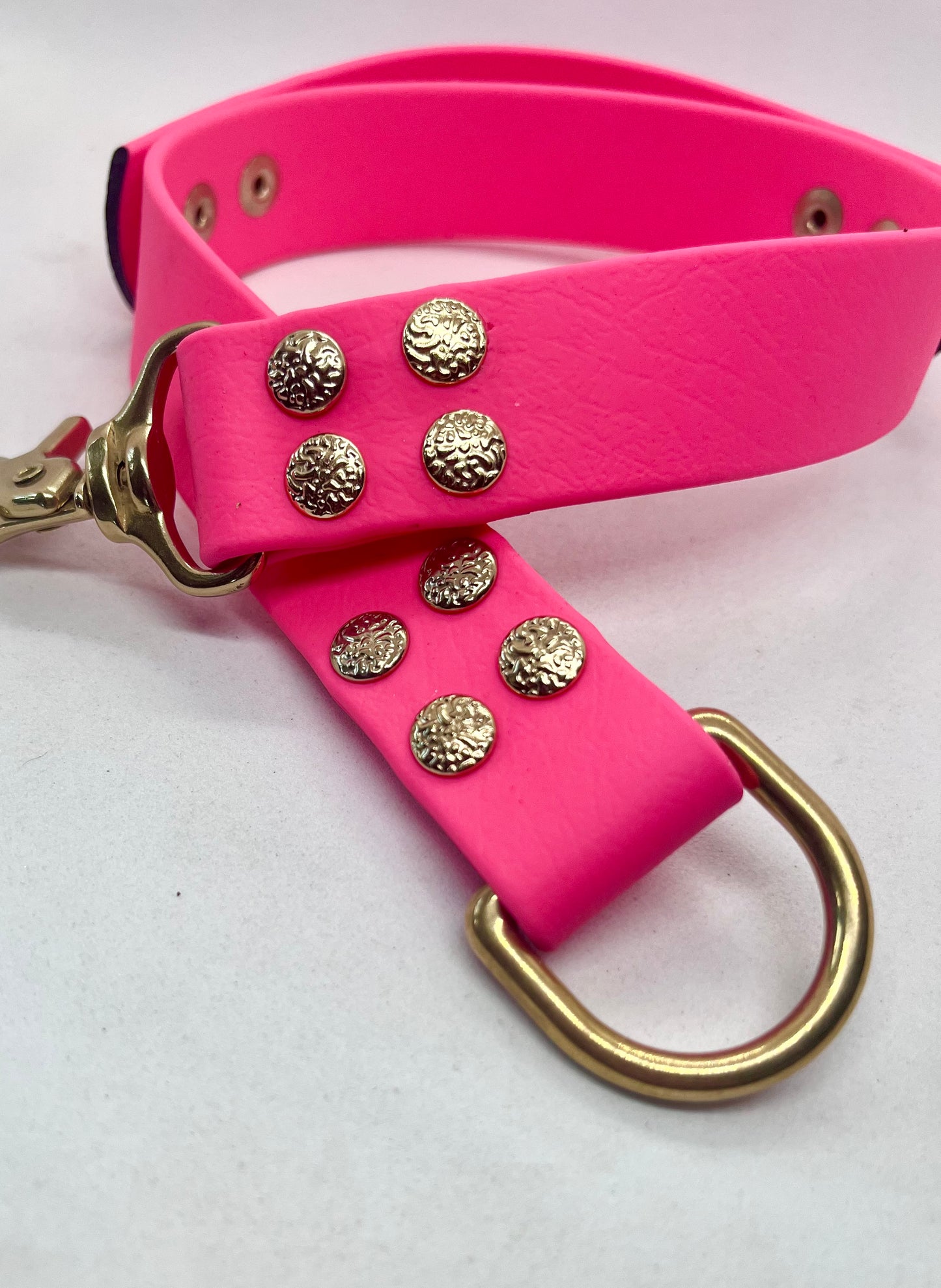 A bright pink faux leather collar with solid brass hardware, featuring textured round studs and a large D-ring. JOOLS LONDON