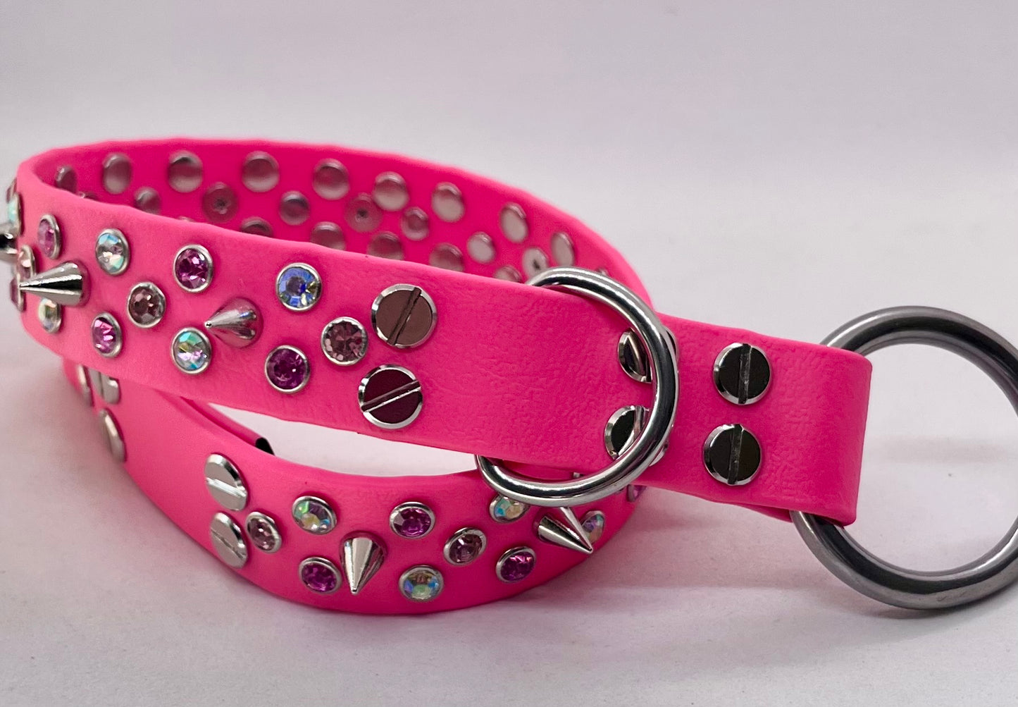 Neon pink rhinestone spiked BioThane dog collar coiled showing stainless steel O ring and D ring hardware